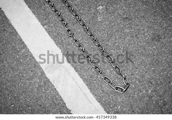 Traffic yellow line with\
metal chain on the asphalt floor - Conceptual background - Black\
and White