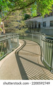 Trail Bridge Over The Picturesque Canal At River Walk In San Antonio Texas. The Paved Pathway Overlooks The Calm Water And Buildings On This Sunny Day.