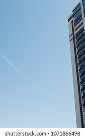 Trail From The Flying Aircraft In The Clear Sky On The Background Of A House With Colored Windows