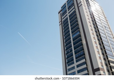 Trail From The Flying Aircraft In The Clear Sky On The Background Of A House With Colored Windows