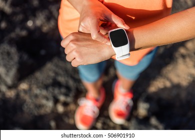 Trail runner athlete using her smart watch app to monitor fitness progress or heart rate during run cardio workout. Woman training outdoors on mountain rocks. Closeup of tech gear.
