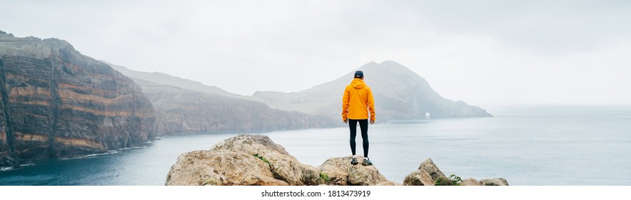 Trail runner man dressed orange waterproof jacket, running tights and shoes enjoying Atlantic ocean bay view on Ponta de Sao Lourenço peninsula -the easternmost point of Madeira island, Portugal - Powered by Shutterstock