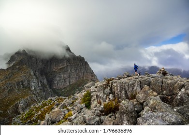 A trail runner running along a steep rocky ridge in the mountains of the Western Cape of South Africa, while a storm moves in over the mountains. - Shutterstock ID 1796636896