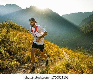 A trail runner running up a mountain trail as the sun rises behind him over the mountain peaks of Stellenbosch South Africa - Shutterstock ID 1700511106