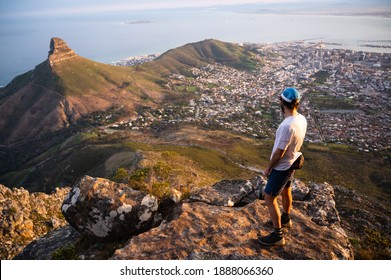 A trail runner standing on the top of Table Mountain looking down at the city and Lions Head at sunset having escaped the busy city. - Shutterstock ID 1888066360