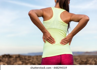 Trail Runner mit schmerzhaften Schmerzen im unteren Rücken oder belasteten Muskel in der Nähe der Wirbelsäule. Weibliche Athleten von hinten auf Outdoor-Run-Presskörper mit Händen für Muskeln Kürbis Kummer.
