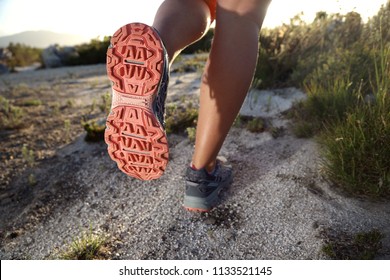 Trail Running Shoe As Seen From The Bottom While A Woman Is Running Outdoors.