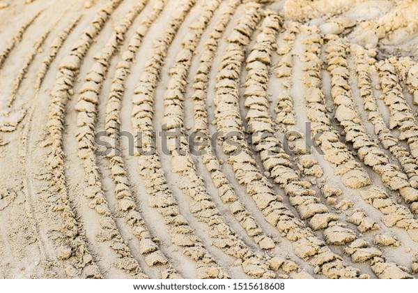 Trail from the tractor in the\
sand ground on the nature outdoors. Texture, background,\
sample