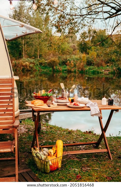 trailer of mobile home or recreational vehicle
stands on shore of pond in camping in autumn near table set,
concept of family local travel in native country on caravan or
camper van and camping
life