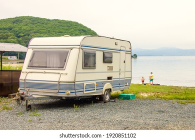 Trailer Motor Home On Beach At Sunset And Family Near It. Tourists Resting Near Camp And Blue Lake  Adventure Relaxing Travel On Caravan Van