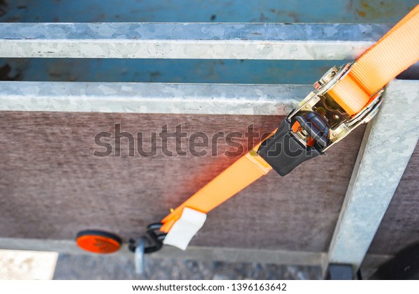 Trailer strop or strap in orange nylon and\
metal, object helping for holding stuff , storage and transport for\
safty and security.
