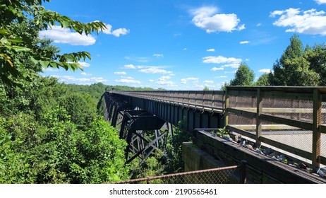 Train bridge spanning river with lush green landscape and blue sky. High Bridge trail is a hiking and bike path in Virginia near the town of Farmville. Former railroad line converted to state park.