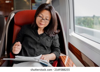 Train Commute Mature Asian Businesswoman Working On Business Trip Commuting To Work. Happy Woman Sitting By Window In Luxury First Class Car Reading Papers