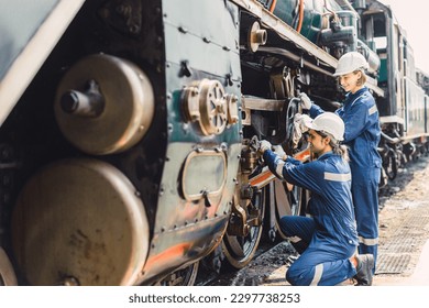 Train engineer team working service maintenance old dirty vintage classic steam engine locomotive in train repair workshop at train station.
