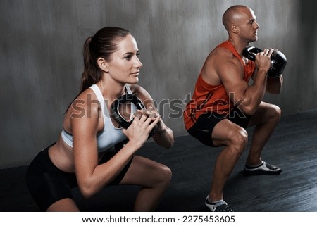 Train insane or remain the same. A man and woman working out with kettle bells at the gym.