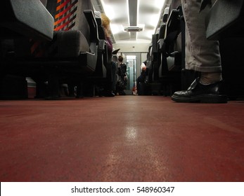 Train interior low angle perspective, from the floor, passengers feet in frame only, red floor
