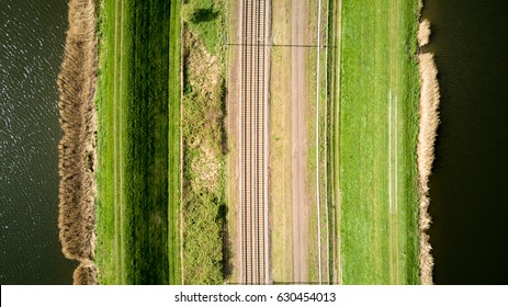 Train Lines. Vertical Aerial Drone View Of A Pair Of Train Tracks Bordered By Water And Pathways Creating Abstract Lined Textures.