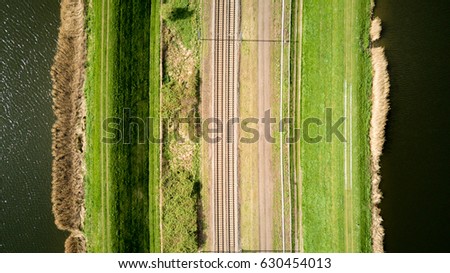 Train lines. Vertical aerial drone view of a pair of train tracks bordered by water and pathways creating abstract lined textures.