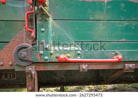 The train is old and rusty, with green paint on the side. The handles on the train are red, and they are located on the side of the train. The train appears to be in disrepair, with the rust