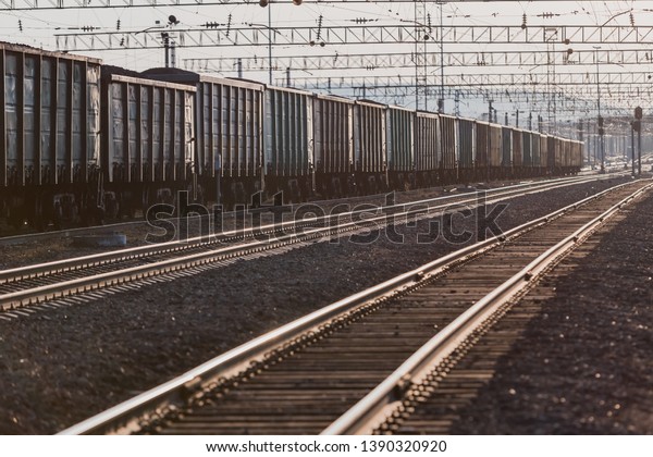 The train is on the railway track. Many\
cars with cargo in the rays of sunset\
lighting.