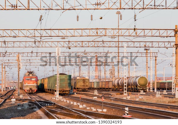 The train is on the railway track. Many\
cars with cargo in the rays of sunset\
lighting.