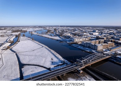 Train passing by steel draw bridge over river IJssel   white floodplains Dutch Hanseatic medieval tower town Zutphen  The Netherlands  Aerial cityscape after snowstorm  