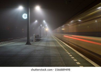 Train passing an empty platform at a railroad station during a foggy night.  - Powered by Shutterstock