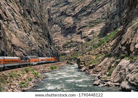 Train riding deep in the royal gorge beside the arkansas river in Colorado. Orange engine beside rushing blue water with rocky cliffs all around