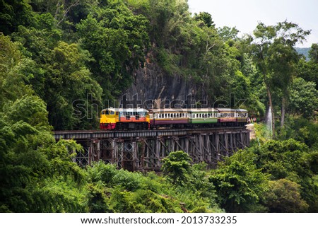 Train running on track between hellfire pass mountain and riverside Sai Yok waterfall and Khwae river bring thai people and foreign travelers travel visit at Tham krasae cave in Kanchanaburi, Thailand