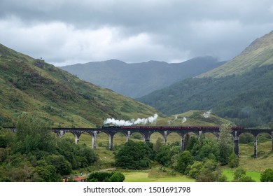 A train with smoke coming out of the stack traveling across a bridge with mountains in the background. 