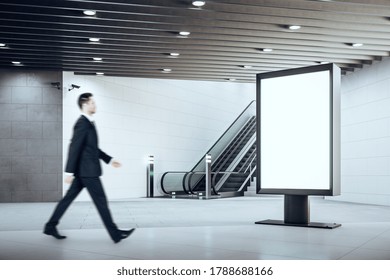 Train Station Interior With Businessman Climbing Escalator And Empty Billboard On Concrete Wall. Mock Up,