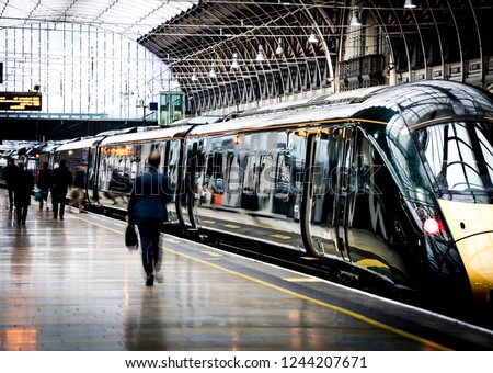 A train station platform with motion blurred people walking