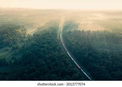 Train In Summer Morning Forest At Fog Sunrise. Aerial View Of Moving Freight Train In Forest. Morning Mist Landscape With Train, Railroad, Foggy Trees. Top Aerial Drone View Near Railway Station.