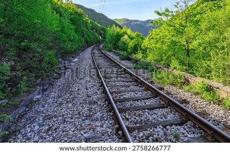 Train track with a mountain in the background. The train is not moving. The train tracks are made of metal and rocks