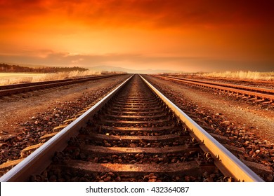 Train tracks goes to horizon in orange majestic sunset.