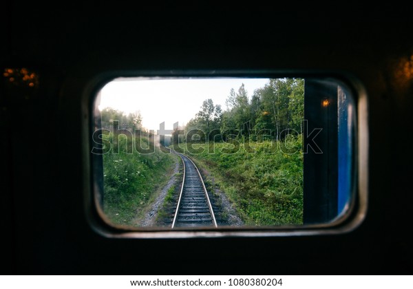 Train travel. Beautiful far scenic view through\
window from riding train at railway with nature ladnscape at\
sunset. Tourist trip. Atmospheric lifestyle journey.  End of\
weekend.  Farewell\
vacation