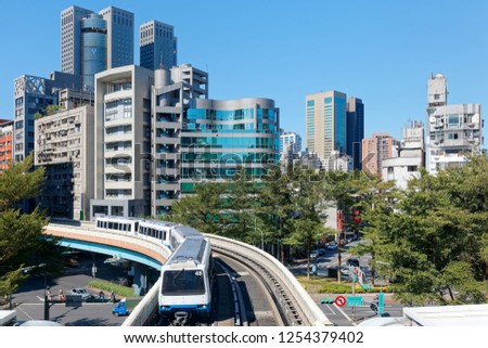 A train traveling on the elevated tracks of Wenhu Line of Taipei Metro System by office towers under blue clear sky~Top view of MRT railways in Taipei, capital city of Taiwan, on a beautiful sunny day