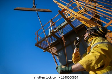 Trained Competent Rigger Wearing Safety Helmet, Work Uniform Using Two Way Radio And Holding A Tagline While Communicating With Crane Operator Load Is Being Lifted Construction Site  Australia