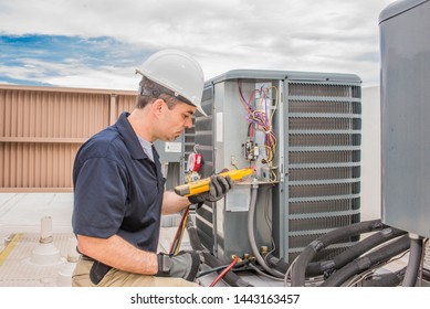 Trained hvac technician holding a voltage meter, performing preventative maintenance on a air conditioning condenser unit. - Shutterstock ID 1443163457