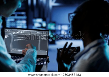 Trained programmers build firewall systems in server room housing advanced infrastructure. Skilled professionals run code on tablet and laptop, to upgrade data center rigs handling demanding workloads