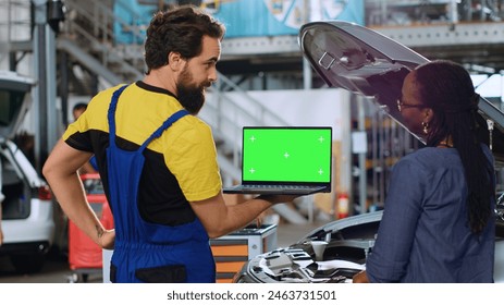 Trained serviceman using green screen laptop in car service to show customer parts needed for busted vehicle. Repair shop worker using chroma key device to search online for auto components
