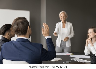 Trainee businessman asking question to mature business teacher on seminar meeting, raising hand, sitting at conference table. Coach giving lesson, consultation to team of professionals - Powered by Shutterstock