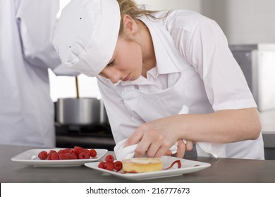 Trainee chef wiping plate of gourmet dessert in commercial kitchen 库存照片
