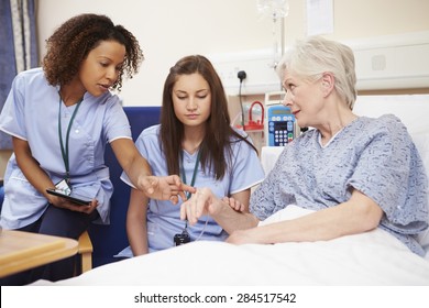 Trainee Nurse Sitting By Female Patient's Bed In Hospital