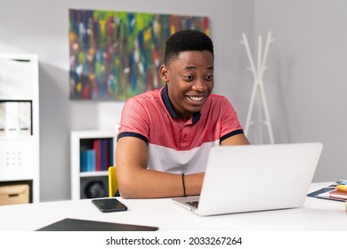 Trainee in office sits at desk in front of laptop monitor in background whiteboard, young dark skinned man talking on internet with clients, co-workers, uses webcam, video call, puzzled surprised face