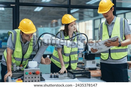Trainees analyze technical blueprint, program, control robotic arm during practical learning lesson in robot system programming at a manufacturing academy. Emphasizing hands-on experience and skills.