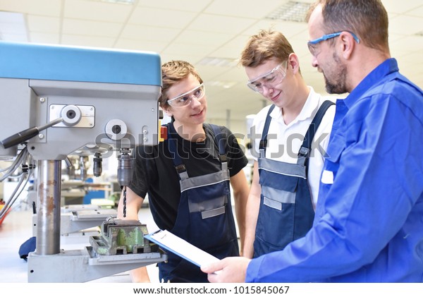 trainer and apprentice in technical vocational\
training at a drilling machine\
