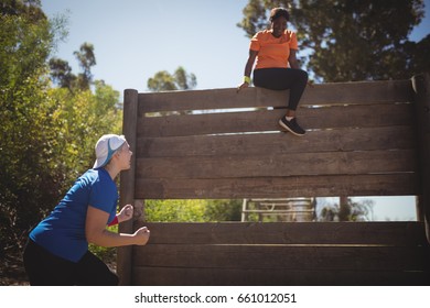 Trainer assisting woman in wooden wall climbing during obstacle course in boot camp - Powered by Shutterstock
