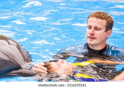 Trainer with boy and dolphin. Treatment of children by means of dolphins. Children and trainer in water petting dolphin. People and dolphins. Concept Dolphin therapy. Kharkiv. Ukraine. 7 15 2018