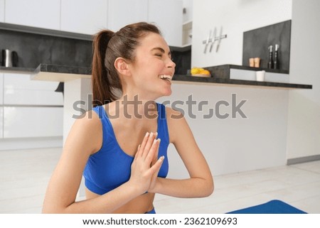 The trainer does yoga asana exercises. Fitness in the flat. A confident aerobics instructor and a healthy lifestyle. A woman does sports. Laughing girl tries to meditate.